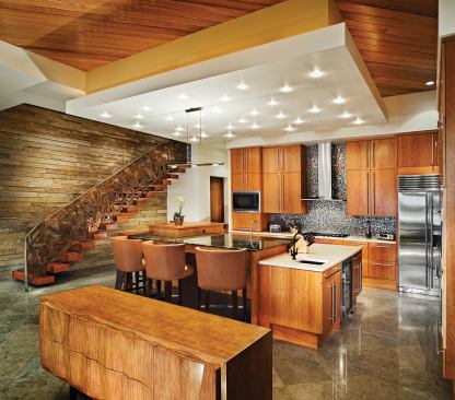 A rough-hewn basalt wall and a sculpted bronze railing contrast with the kitchen’s smooth surfaces of polished wood and stone. Overhead, a dropped, downlit ceiling resembles a star-filled sky.