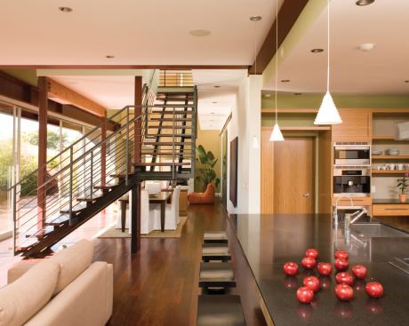 An open-riser steel stair forms a light and permeable boundary between the living room and kitchen seating area.