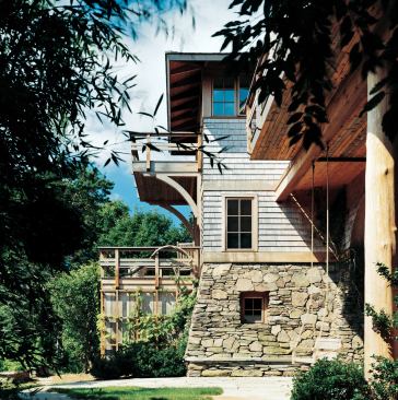 With its rambling, asymmetrical plan and natural exterior finishes, this house seems as rooted in its site as the trees that surround it. In fact, due to a high water table, its battered stone walls rest on a network of pilings.
