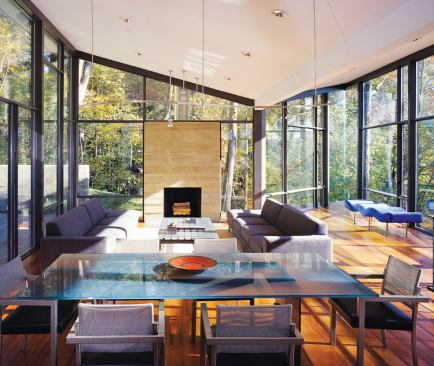 The living room fireplace and board-formed concrete chimney supply a solid, anchoring presence against the transparent glass walls.
