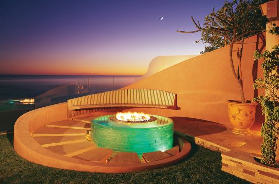 A circle of fire set within a circle of water that trickles over the stacked glass walls of this fire pit warms body and soul on cool seaside nights. Curled around the fire pit, a stucco wall supports a teak bench and steps that seem to float above the water.