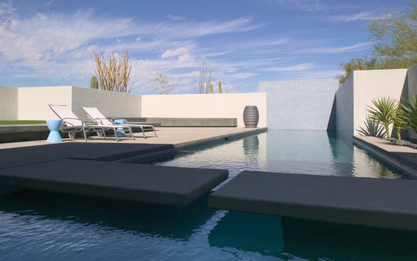 Two sides of the pool rise up out of the water and become perimeter walls, an architectural move that adds to the feeling of simplicity and serenity.The blue mosaic tiles reflect the color of the sky and give the water a more refreshing hue.