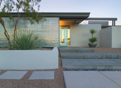 Deep overhangs help shade the main entry while a corrugated galvanized steel wall doubles as privacy screen and backdrop for an elevated planting area. Deep, shallow steps draw people in from all directions.