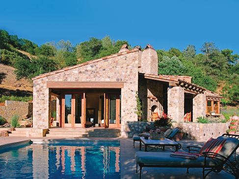 Custom bi-fold doors extend the living room to the concrete loggia and outdoor fireplace and open the bedroom to the pool deck, where views of nearby vineyards and the distant Napa Valley give this small home a sense of great expansiveness. 