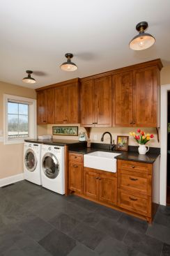 Custom cabinetry, granite countertops, a farmhouse sink, slate flooring and oil rubbed bronze hardware give this utility room designed by Crystal Kitchen + Bath a sophisticated, warm and welcoming feel to the family and friends who enter the home from this secondary--yet more often used--entrance.