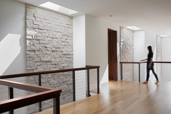 Atop the natural stone foyer stair, sheltered privacy for the three bedroom suites is found in the Guest Lounge. The movement set by the wooden railings creates a rhythm with the rising natural stone walls that give way to skylights for natural light. The Guest Lounge appears to float as it vertically connects to the foyer and dining with openings to the lower level.