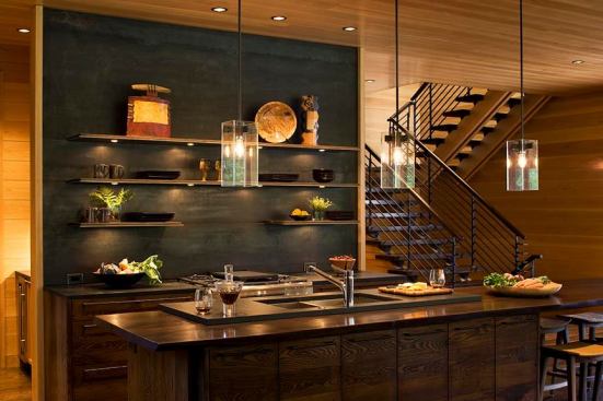 A wall partition covered in sheets of blackened steel provides a nice counterbalance to the walnut island countertop and wormy chestnut cabinets in this Asheville, N.C., kitchen. Designed by Carlton Architecture as an open pavilion, the main workspace hides waist-high appliances such as the oven and dishwasher behind the island, and sticks with a downdraft ventilation over the range so as not to interrupt the backsplash wall’s clean lines. Taller units—the fridge, wine storage, and microwave—are tucked into a pantry alcove around the corner. 
www.carltonarchitecture.com