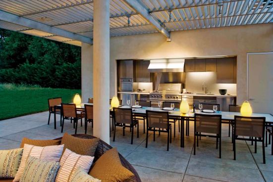 The metal overhead grid shades the kitchen and edges of the east/west-oriented pavilion, its slats angled to block direct sun during the day.