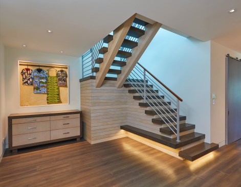 The stairwell brings in natural light from monitor windows above into the center of the house and provides a focal point at this main circulation juncture. A custom cabinet blends with the stair and a barn door on the right discretely closes the large butler’s pantry from view.