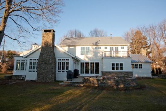 The house's rear elevation and patio. A stacked-stone wall encircles a firepit.