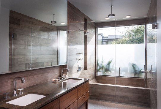Here, the bath tub is contained within the glass-walled shower. A ceiling height picture window that's frosted lets the outdoors in while ensuring privacy. 