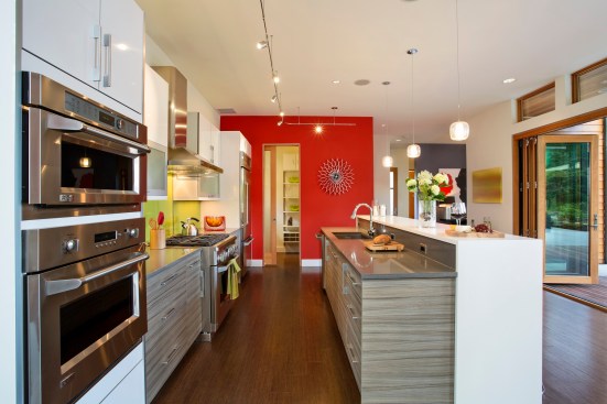 Both the red wall and lime-green backsplash in this kitchen provide colorful focal points in a small space. Project: EVOKE-LUXE by Quadrant Homes 