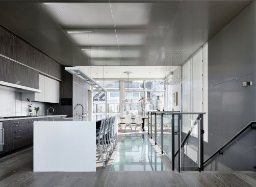 A perforated metal screen wraps the kitchen ceiling and down along the stairwell wall to the entryway. Skylights and an etched glass floor funnel light into the center of the house.