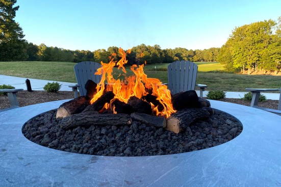 The fire pit at Fawn Lake Country Club, designed by Warming Trends, has a 48-inch-diameter flame within a 90-inch-diameter pit filled with lava rock and realistic ceramic logs. The outside of the fire pit is finished with hard scape to match the clubhouse.