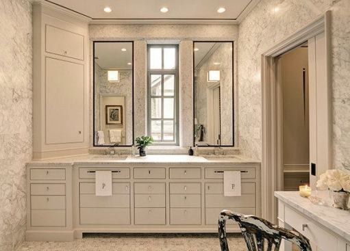 As part of the second phase of a whole-house remodel, DeRhodes Construction redesigned this master bathroom, incorporating custom features and details. On the marble wall of the vanity, two piece mirrors border a narrow window. The team mitered, beveled, and fabricated marble to give the impression of large columns and beams. Below, custom, hand-painted cabinetry provides storage.