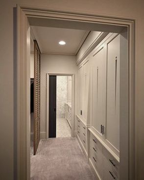 The walkway to the bathroom features a custom linen press cabinet and cypress louvered doors separating the walk-in closet.