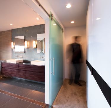 This frosted glass pocket door adds texture without distracting from the bath’s soothing palate. Opposite, a tricked-out wall slides open with two doors that reveal a closet, turning a small space into an efficiency workhorse. Designers at Stephen Jenkins Design-Build were careful to eliminate any unnecessary hardware, allowing surfaces to blend together.