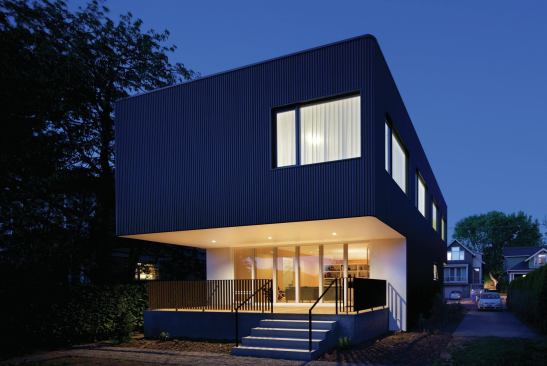 Low cost and low maintenance, corrugated metal siding wraps the corners and window recesses of the upper volume like a sleeve, eliminating the need for trim.