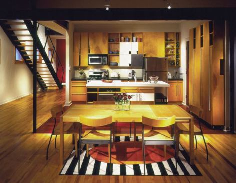Cutout handles and casters on birch plywood cabinetry elevate budget-conscious material in this architect’s own kitchen. A splurge on Brazilian cherry flooring underscores the kitchen zone within the larger, maple-floored room.