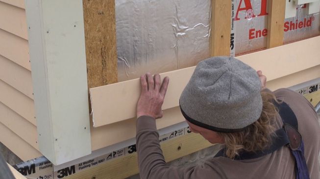 A carpenter sets a clapboard over a drainable air gap.