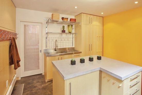 The center island is topped in concrete and houses a refrigerator and freezer drawers, as well as plenty of storage. Behind the island is a durable stainless steel clean-up sink and rack with custom cabinets below. 