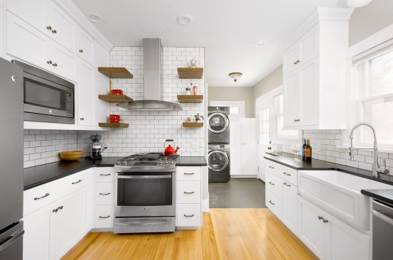 WIth little room with which to work, Renaissance Remodeling incorporated the laundry room area that sits behind this kitchen into the overall design. Subway tile with gray grout, black granite countertops and black/stainless steel appliances help to complement the washer and dryer while black marmoleum floor unifies the two separate spaces. 