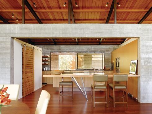 The kitchen is bounded by two parallel walls of board-formed concrete.