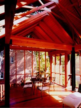 A delicate web of 2x4s braces the porch's gabled roof. The peaked roof is topped by a long custom skylight that lets shadows and light filter through surrounding branches and dance into the space.