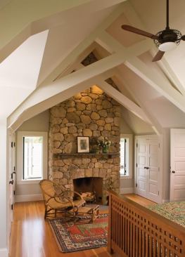 Soaring ceiling, exposed trusses, and stone fireplace give the master bedroom a sense of presence and solidity. 