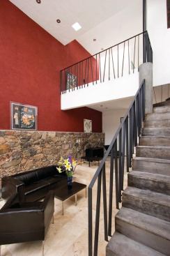 Made with local labor and materials, interiors feature travertine floors, a continuous red accent wall, steel railings, whitewashed surfaces, and an old stone wall.