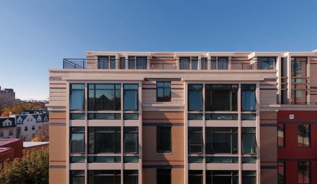 Four vertical rows of bay windows, modern dormers, staggered building tiers, and a light color brick with dark accents give a hat-tip to the old buildings that surround this new one. 