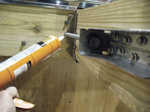 To keep out water and insects, the author caulks all holes drilled through the house. Note that he installs the brackets 6 to 8 inches away from ledgers, rims, and other framing members. The distance makes it easy to caulk holes in the rim joist, as well as access the brackets with a wrench or drill.