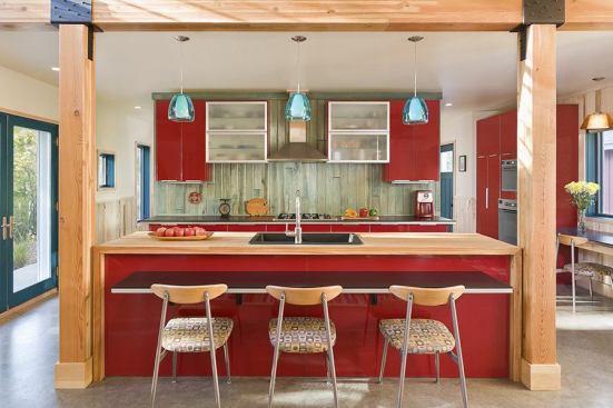 A straight-on view of The Red Cottage's kitchen shows off shiny red cabinets and glulam beam framing, and a playful use of color and materials.. 