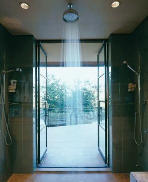 The oversized overhead rainfall fixture is centered between the terrace doors, which open wide to the great outdoors.
