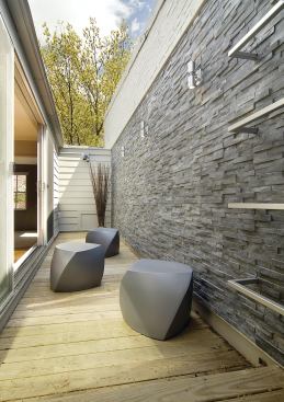 The courtyard floor is covered with ipe decking. An exterior stone wall provides contrasting texture. The stainless steel ladder (far right), attached to the exterior stone, provides access to a modest roof deck.