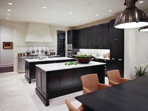 Dual islands allow for multiple cooks and entertaining stations. The far island features an ice maker, wine cooler, and stools. The limestone tile flooring provides a contrast to the wood floors used in the rest of the house. The countertops are made of Calacatta honed marble.