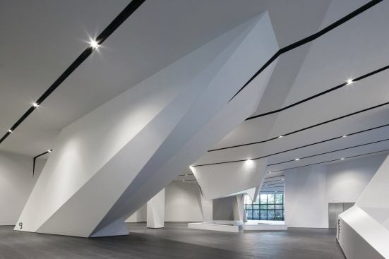 The ground floor forms a sort of hypostyle hall, with the articulated ceiling plane extending to the ground to encase columns, elevators, and escalators. The stone tiles that line the space are part of the flooring detail system designed by NADAAA, which aims to continue the exterior plaza into 

the building.