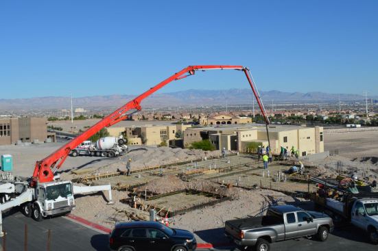 A pump truck flows concrete to the back of the house for deepened footings near the pool.
