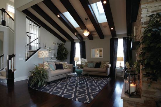 The two-story great room showcases a vaulted beamed ceiling, two solar-powered skylights, a gas fireplace with floor-to-ceiling stone detail, and transom windows to bring in natural light.