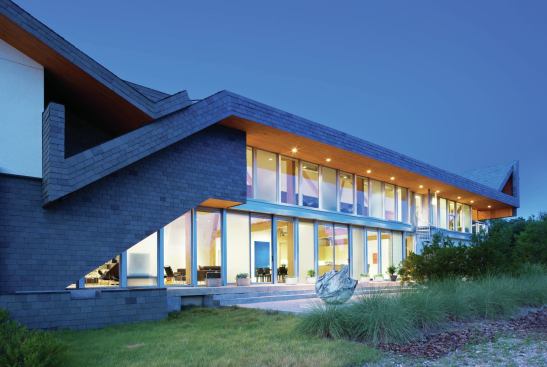 The southern facade of the house is open wide to the side yard, with rows of sliding glass doors and windows that create bright, lofty interior spaces.