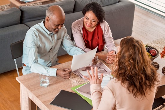 Mature couple looking photographs while discussing with female interior designer at home.